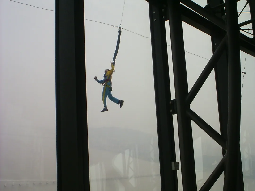 Bungee jumper on cord below tall tower with scenic view